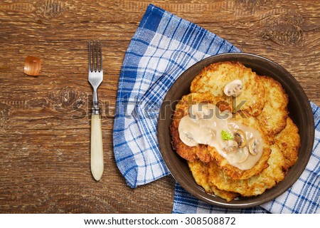 Homemade potato pancakes served with mushroom sauce and mushrooms on wooden board.