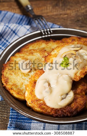 Homemade potato pancakes served with mushroom sauce and mushrooms on wooden board.