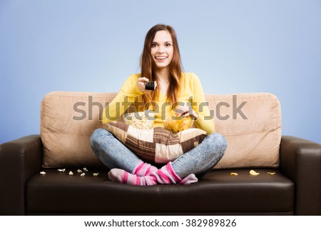 Young woman spends his free time watching TV on the couch at home, munching chips and popcorn. Gray background, easy to remove.