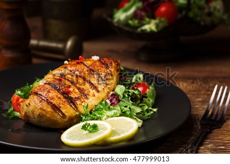 grilled chicken breast with green salad and french fries on a black plate.