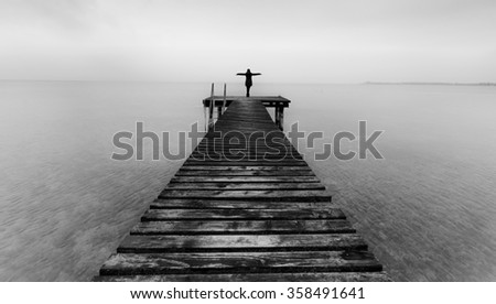 Woman standing on a wooden jetty. Woman on a pier on the lake greeting the sea with arms wide open.