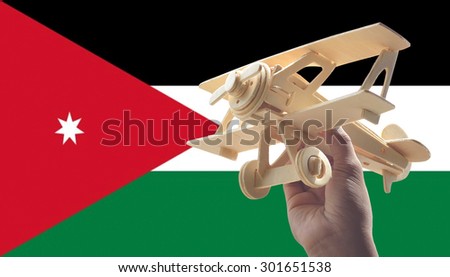 Hand holding airplane plane over Jordan flag, travel concept
