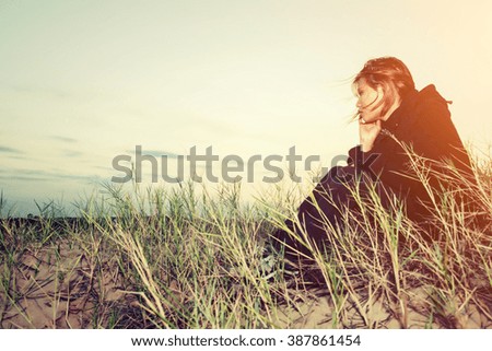 Sad young girl sitting alone on a grass outdoors,Sadness. Loneliness
