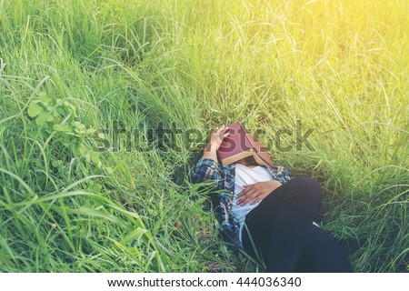 Young hipster man lying down on grassland napping tired after reading book with nature around.