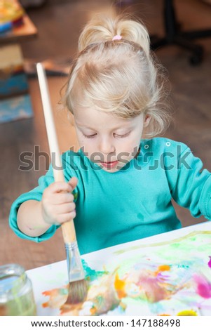 Little cute blonde girl drawing with watercolor paints