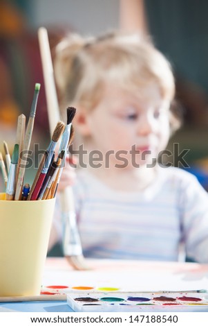 Little cute blonde girl drawing with watercolor paints