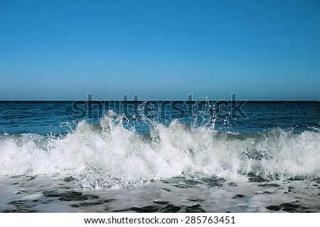 Ocean tidal waves breaking on a sand beach splashing under clear blue sky