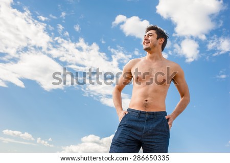 Fit handsome healthy athletic young happy man with bare torso standing under scenic blue sky on sunny day. Concept of recreation, healthy lifestyle and well being.