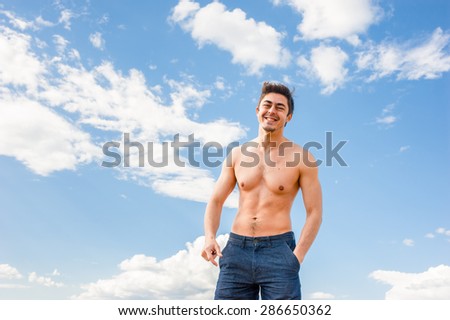 Fit handsome healthy athletic young happy man with bare torso enjoying life under scenic blue sky on sunny day. Concept of recreation, healthy lifestyle and well being.