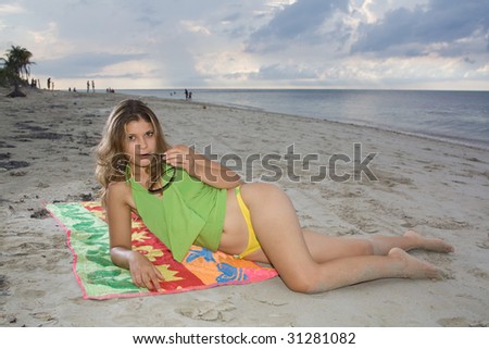 Pretty girl with yellow bikini laying on a towel, with sunglasses in the hand