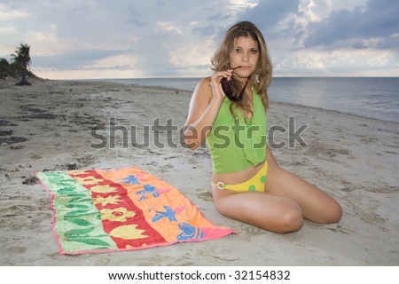 Attractive lady sitting on a towel with green blouse and holding sunglasses
