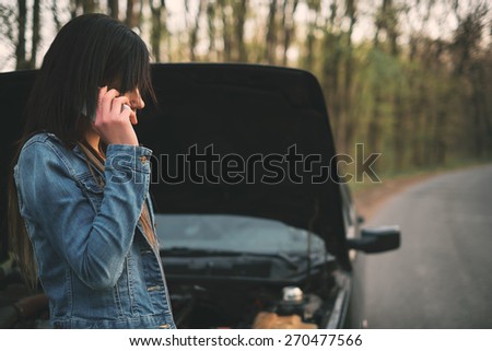 Young caucasian woman with brown hair under the hood of her car break down