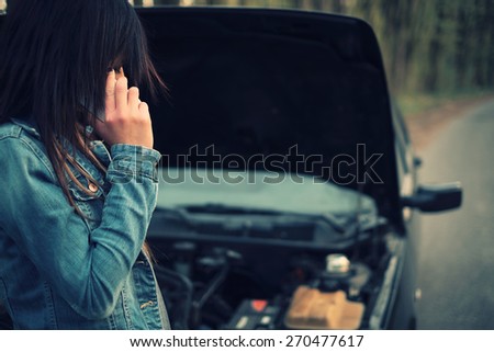 Young caucasian woman with brown hair under the hood of her car break down