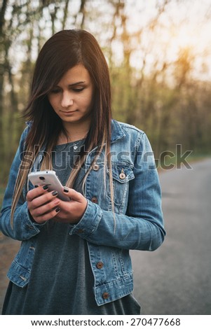 Young brunette girl messaging smart phone on the park
