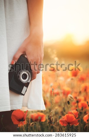 Vintage camera in woman hand on poppy field