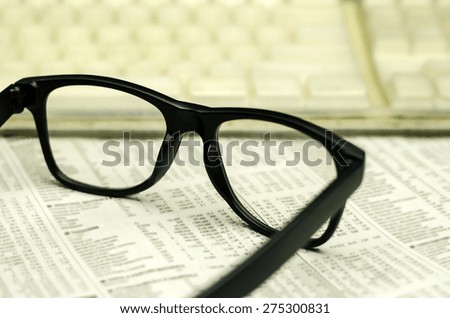 keyboard and a black eyeglasses on a financial newspaper with a very shallow depth of field with copy space for text