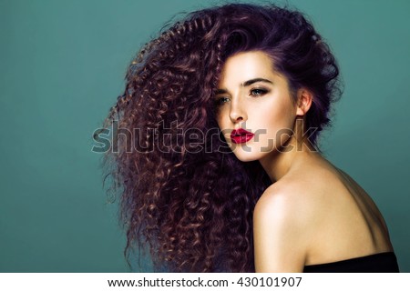 Beauty young woman with curly big and long hair. Permed hair. Glamour lady, Beauty Girl on blue background. Beautiful Woman Portrait. redhead Wavy Hair, perfect make up, red lips, thick eyelashes.