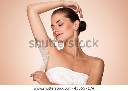 Armpit epilation, hair removal. Young woman holding her arms up and showing clean underarms, depilation smooth clear skin . Beauty portrait. armpit\'s care. Large white feather near skin