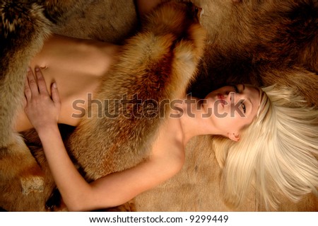 beautiful blond woman barely under furs lying on fur rug with hair fanned looking up seductively
