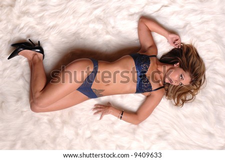 very sexy young woman in blue bra and panties lying on white fur rug with hair fanned out looking seductive