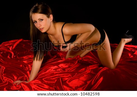 seductive young woman on hands and knees on red satin sheet with black background