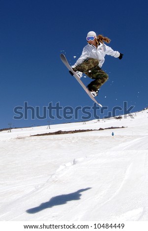 woman snowboarder in air flowing jump holding board with sky and shadow.