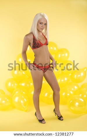 beautiful blond woman in red bikini bending with yellow balloons on yellow background full body