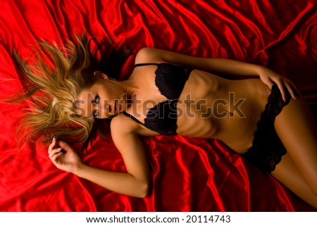 Beautiful blond girl in black bra and panties lying on a red satin-sheet