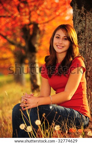 pretty brunette girl sitting in front of red maple trees in fall color with matching top