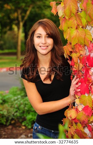 pretty brunette girl leaning against fall ivy with reds and yellow leaves.