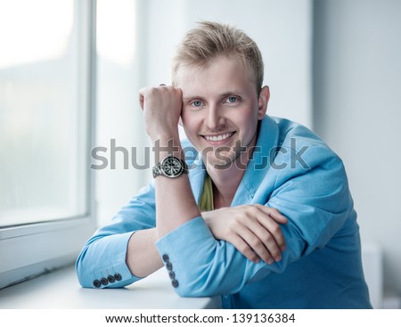 portrait of the handsome young man in a blue jacket at a window