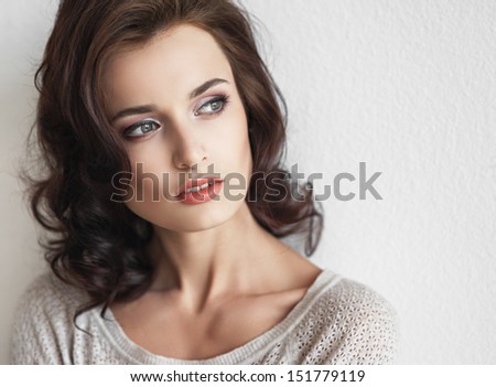 Portrait of the beautiful young fashionable girl with brown hair in studio posing against a white wall