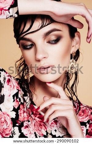 Fashion photo of beautiful model  in elegant dress and gold accessories posing on brown background