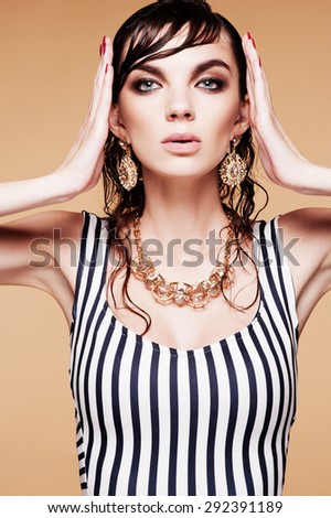 Fashion photo of beautiful model  in elegant dress and gold accessories posing on brown background