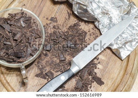Chopped chocolate pieces on a wooden cutting board. Near packaging foil. From the series \