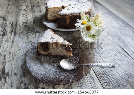 Slice of Cheesecake on an glass plate with a bouquet of daisies and a form for baking. Retro style. From the series \