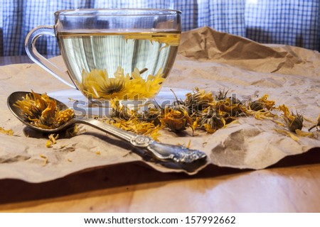 Glass cup of herbal tea. Near teaspoon dried marigold flowers and on the packaging paper.