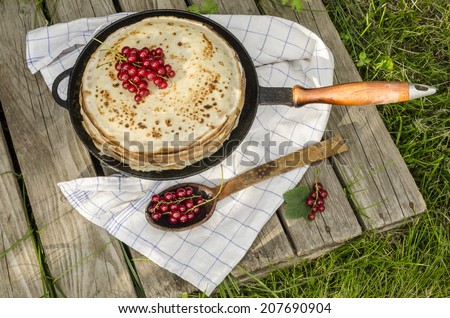 Pancakes with red currants on old pan. Near wooden spoon and kitchen towel. From series Summer desserts