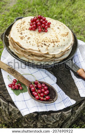 Pancakes with red currants on old pan. Near wooden spoon and kitchen towel. From series Summer desserts