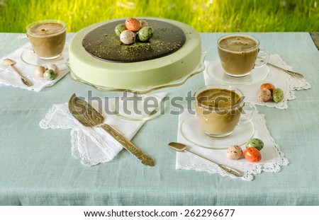 Easter table with tea matcha cheesecake and white coffee on background of green grass. Near sweet-stuff eggs. From series elegant desserts