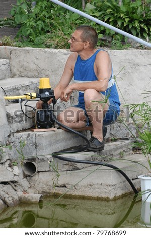 A man with the electric water pump for watering garden near pond.Near Kiev,Ukraine