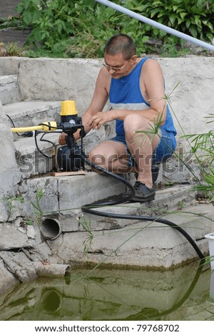 A man with the electric water pump for watering garden near pond.Near Kiev,Ukraine