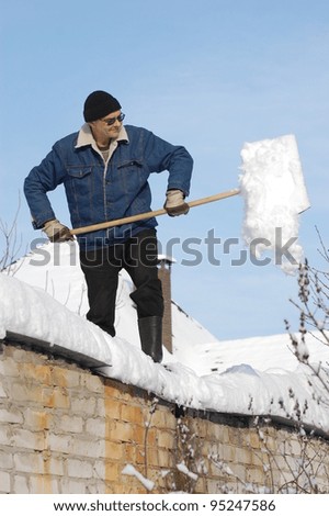 A man with a shovel removing snow from a roof . Near Kiev,Ukraine