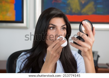 Beautiful business woman applying makeup in office