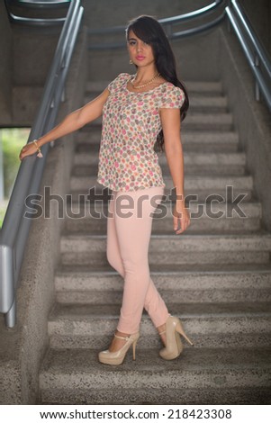 Woman standing on staircase,  wearing  stamped blouse and light pink  pants