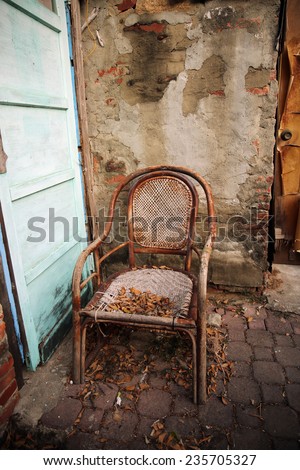 Old wicker chair near stony wall in fallen leafs.