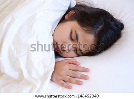 Cute young girl sleeping on a bed with white blanket and pillow.