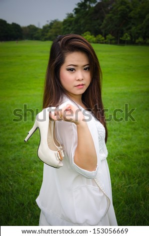 Beautiful young woman holding shoes, meadow background.