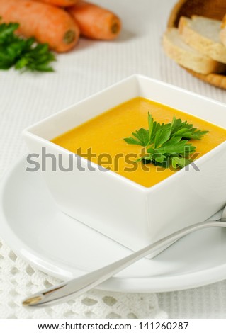 Carrot soup in white bowl with carrots and parsley in the background