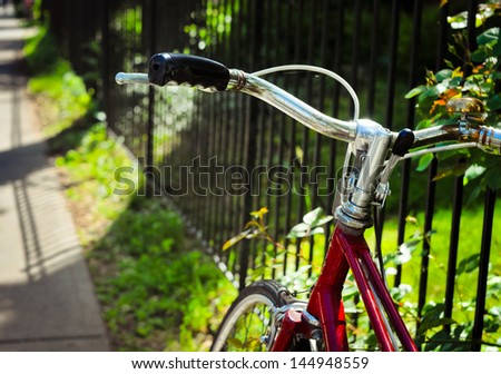 Handle bar of a red bicycle with black grip, bronze bell. near steel bar fence